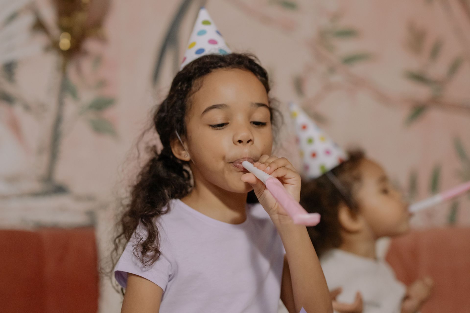 Two young girls in party hats enjoying a birthday party indoors.